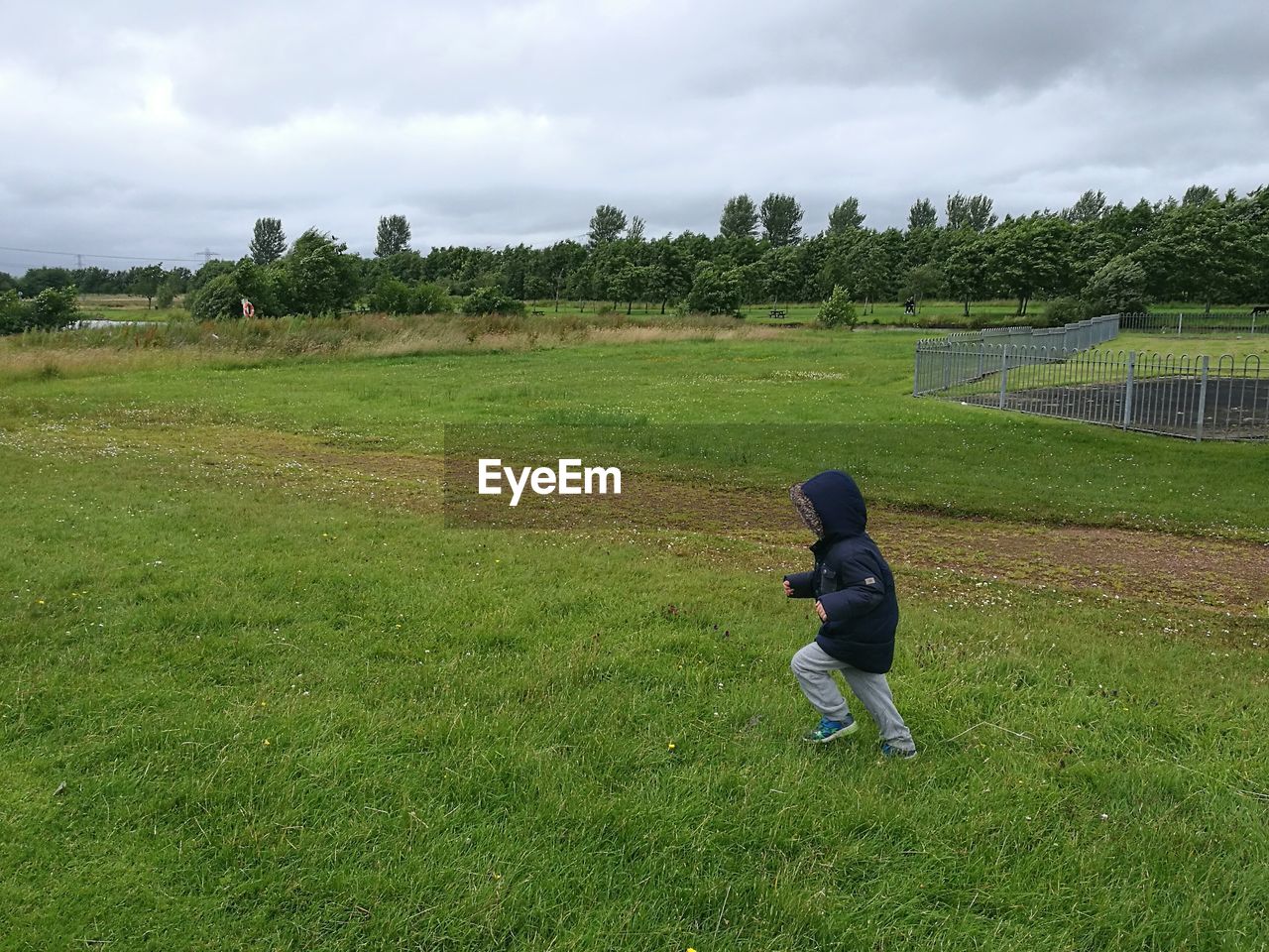 Boy in hooded shirt running on grassy field against sky