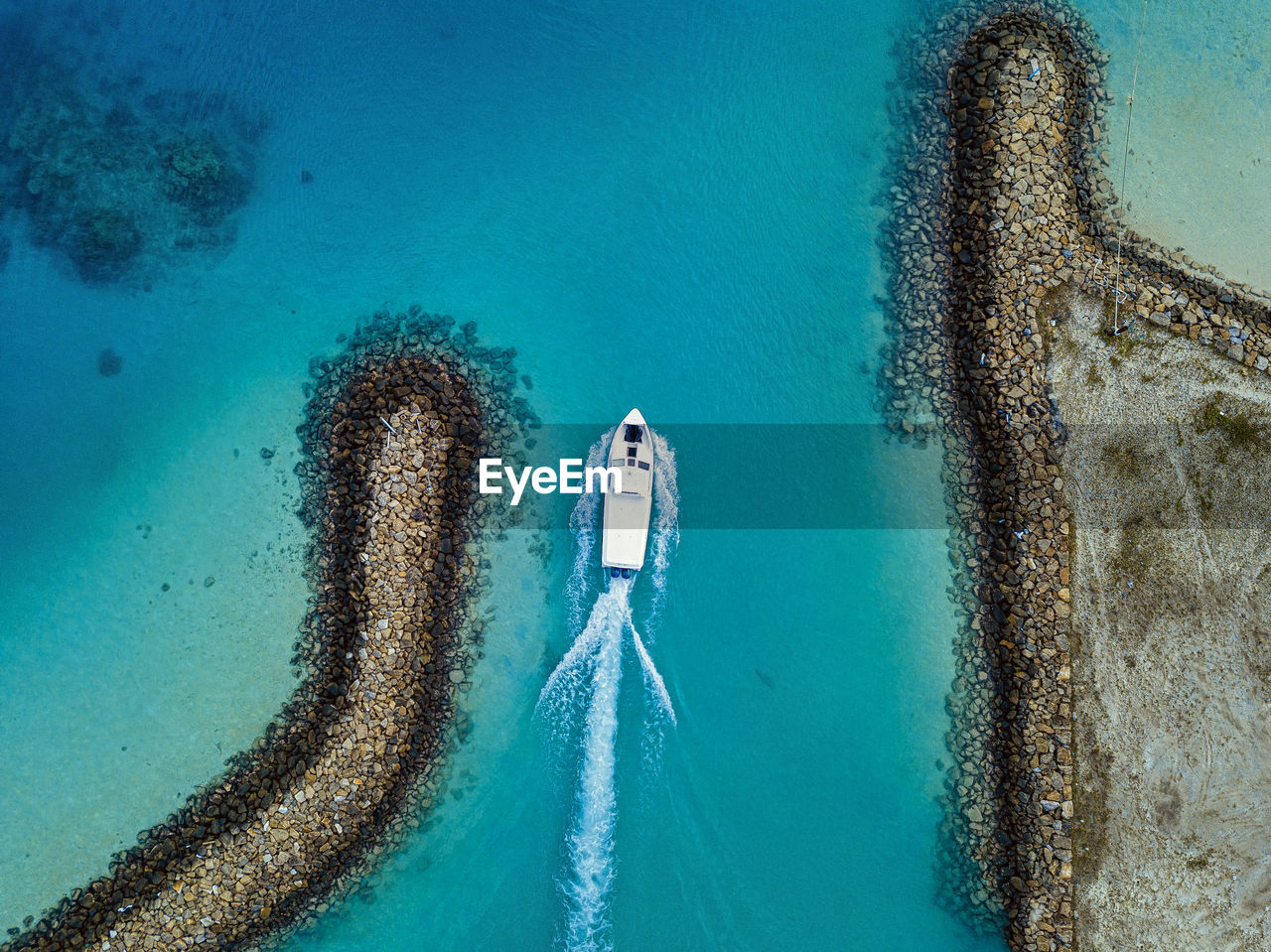 Aerial view of boat sailing past retaining walls of thulusdhoo island, maldives