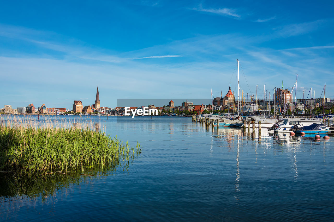 SAILBOATS IN RIVER BY BUILDINGS AGAINST SKY