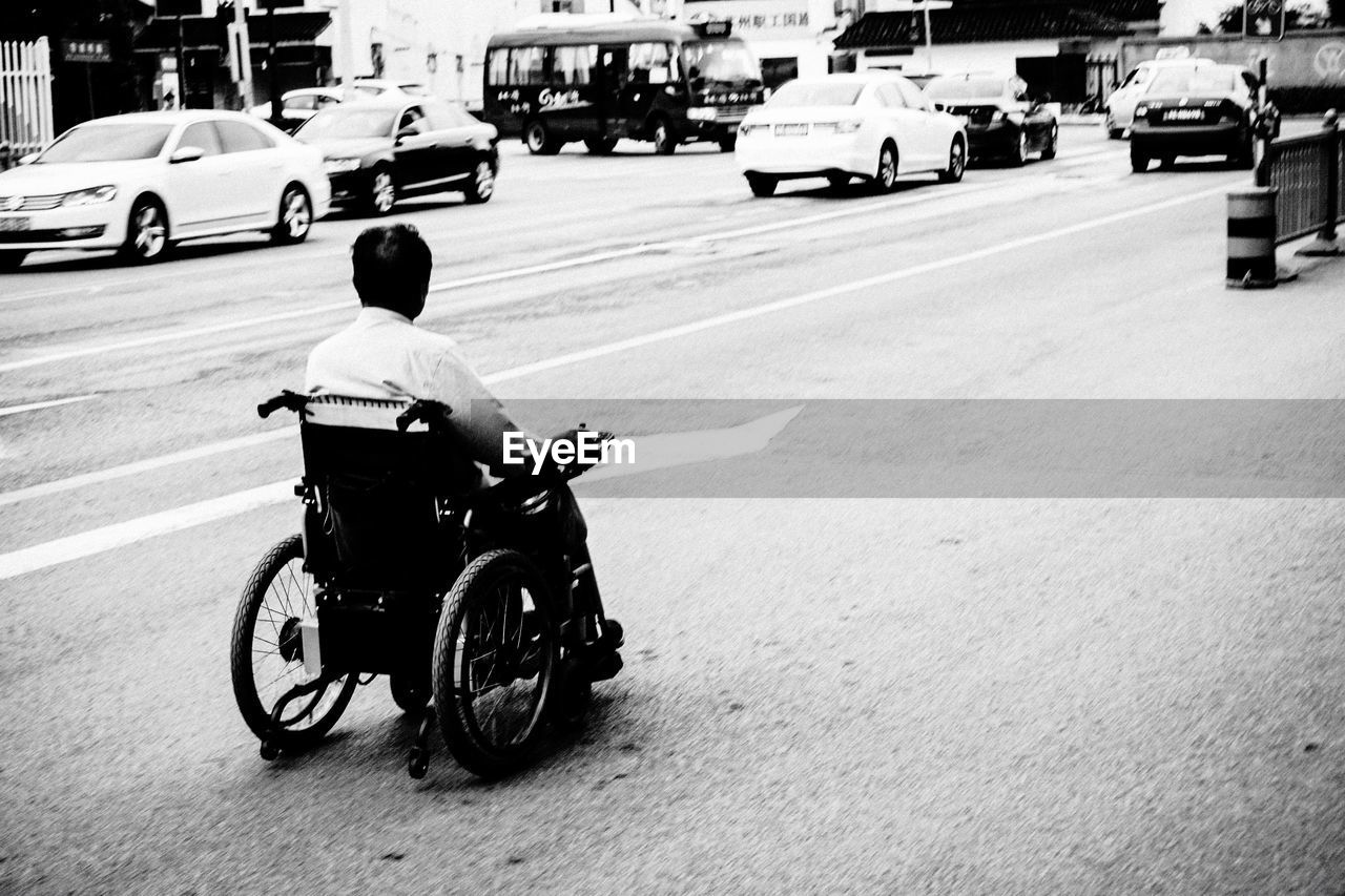 Man in wheelchair on road by cars at city