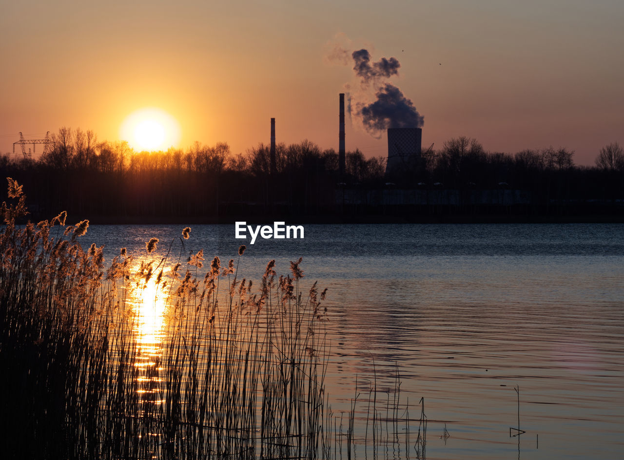 reflection, sunset, sky, water, dawn, evening, nature, sun, beauty in nature, silhouette, plant, lake, tranquility, sunlight, tree, scenics - nature, cloud, orange color, tranquil scene, horizon, no people, idyllic, afterglow, architecture, outdoors, environment, landscape, light, back lit, built structure