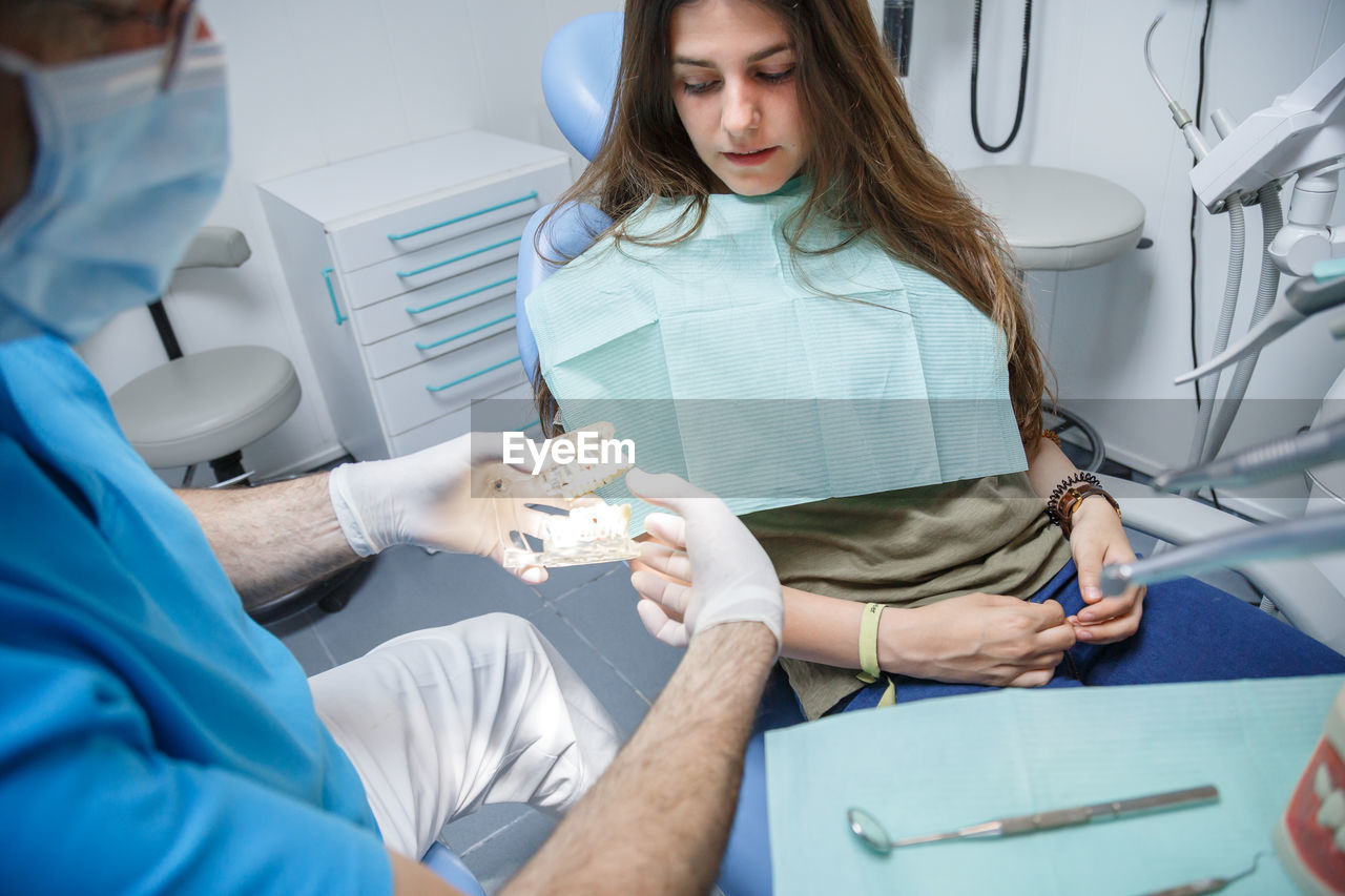 Midsection of dentist holding dental equipment by patient in clinic