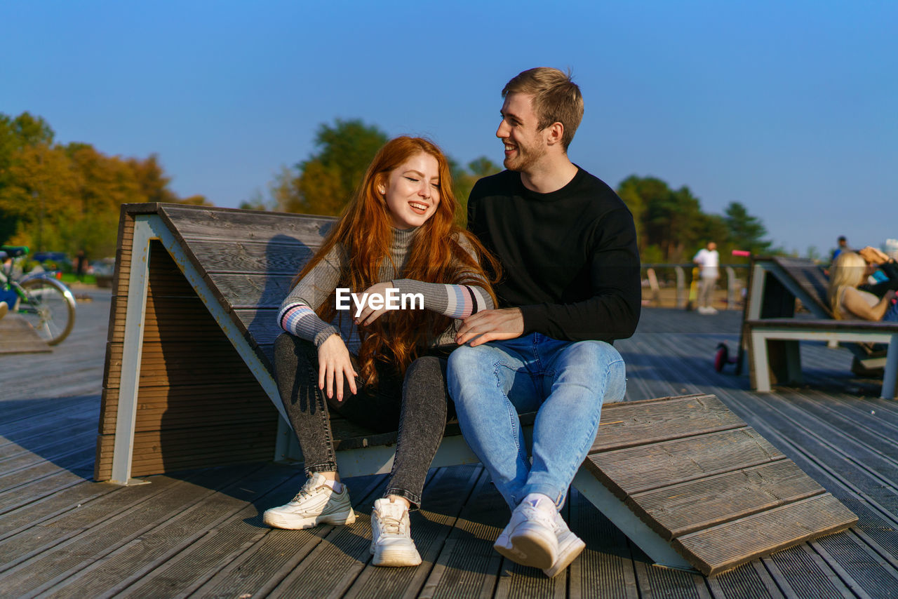 Young couple are sitting in the park on a wooden bench hugging person