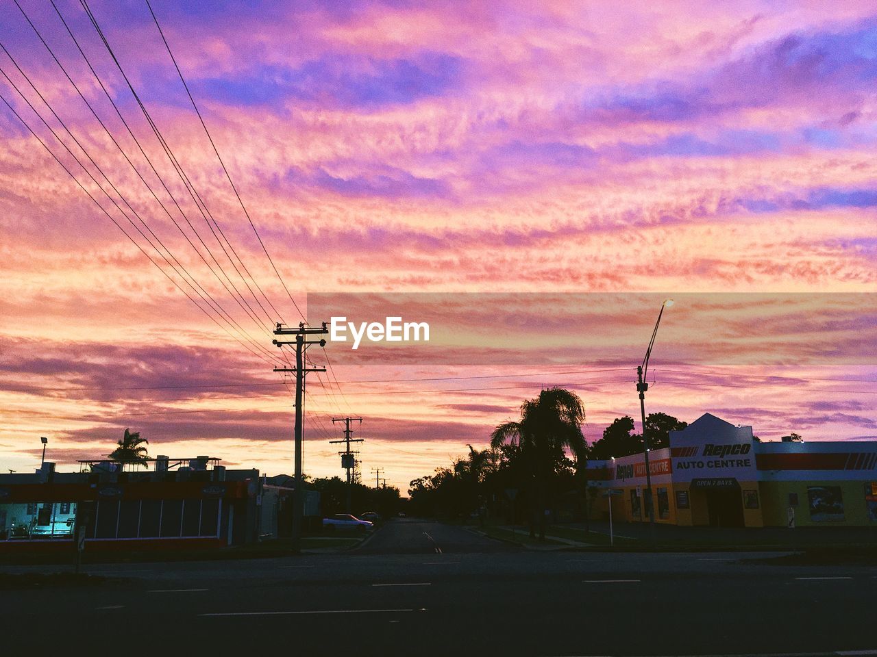 Street by silhouette buildings against dramatic sky