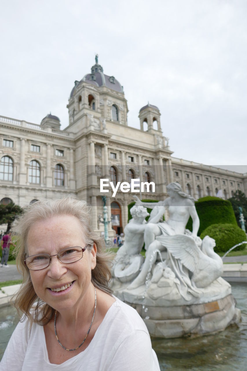 Smiling mature woman standing against statues at hofburg palace