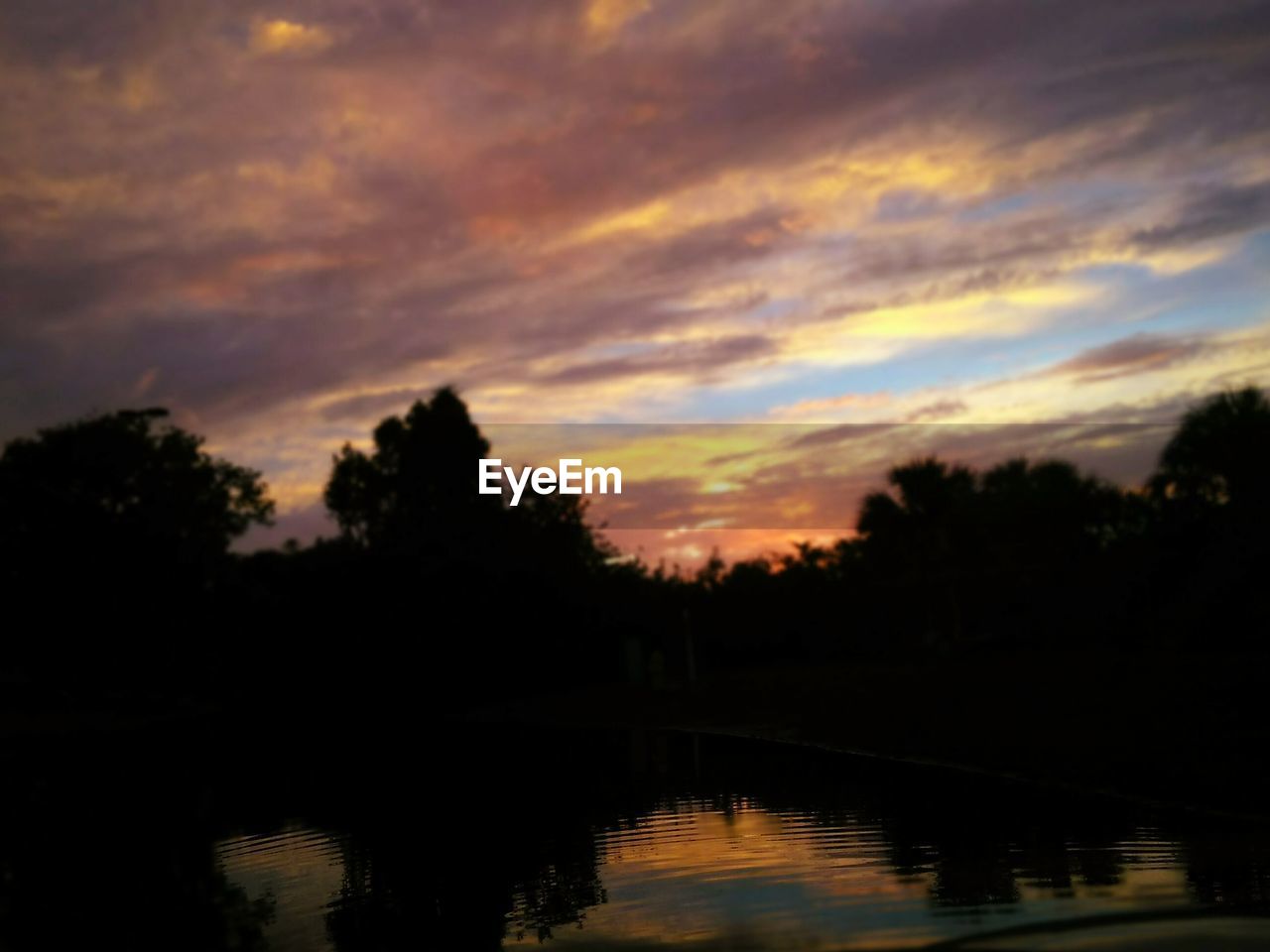 REFLECTION OF SILHOUETTE TREES IN LAKE AGAINST SKY DURING SUNSET