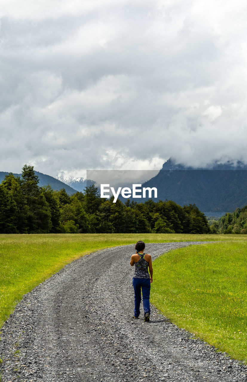 Rear view of woman walking on road against cloudy sky