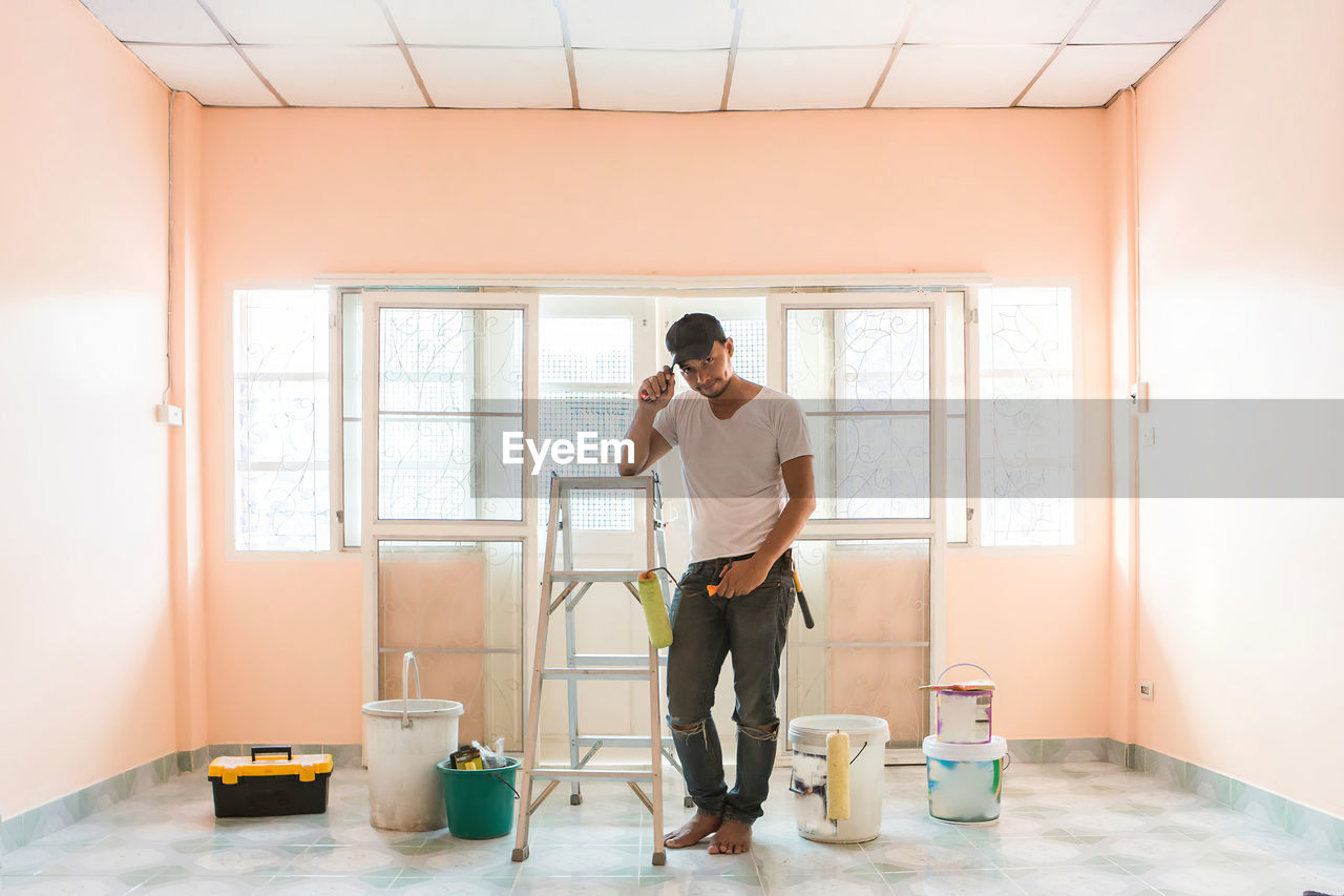Worker man repairing a house with tools and paint the pastel orange room, the green tiled floor.
