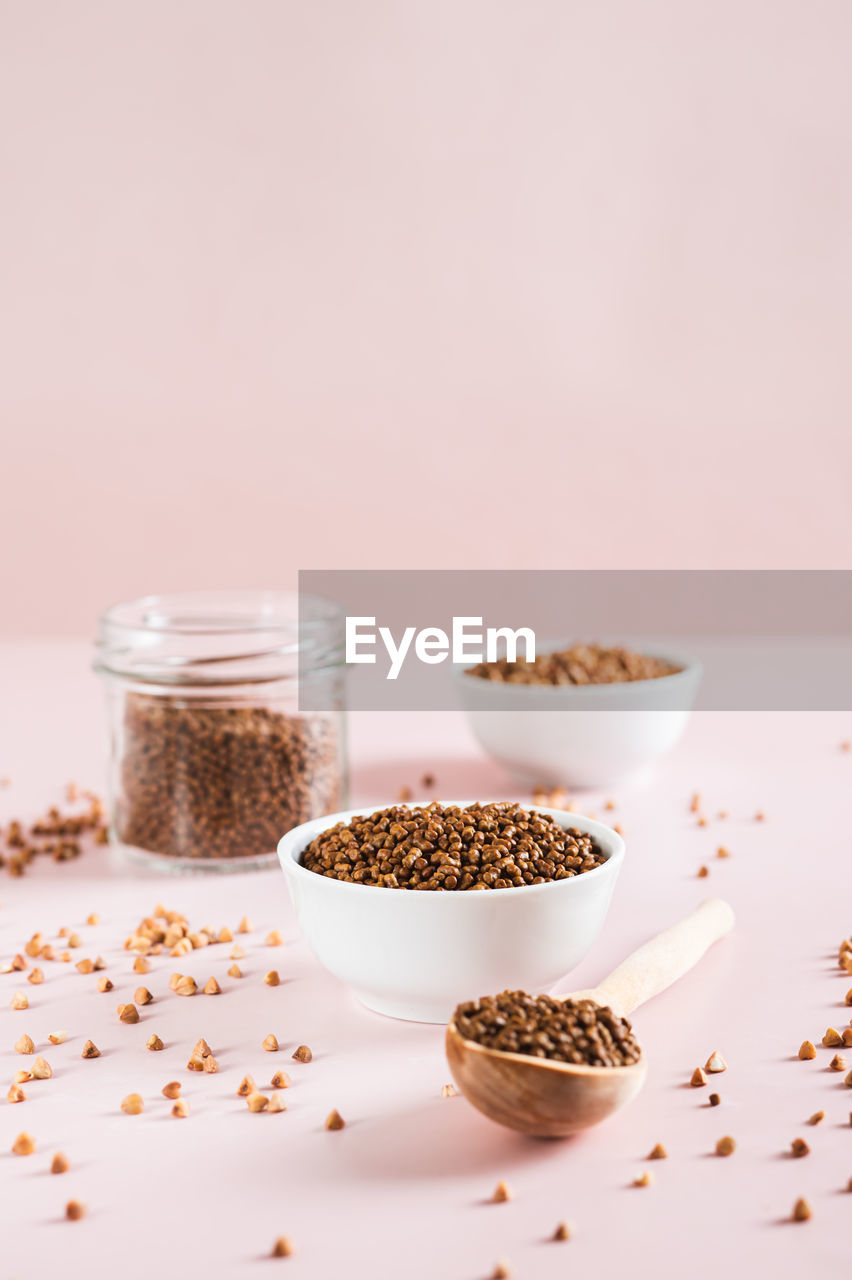 Dry buckwheat tea granules in a bowl, spoon and jar on the table vertical view