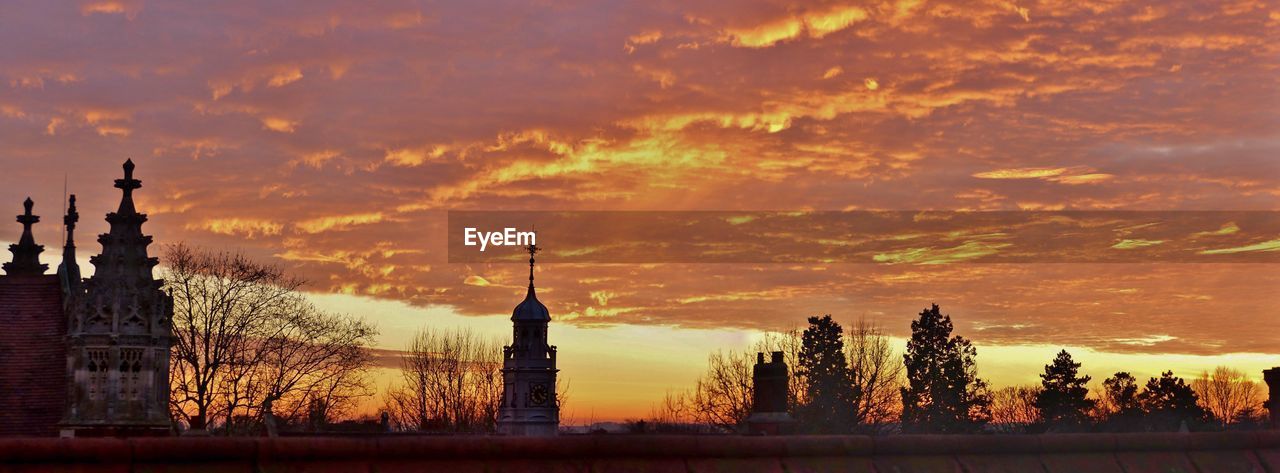 Panoramic view of silhouette buildings against cloudy sky at sunset