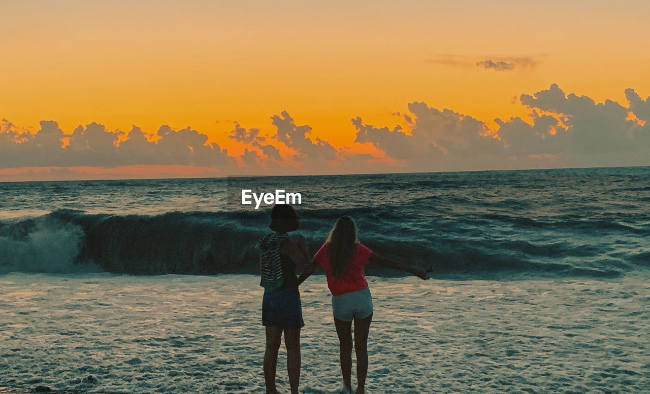 Sea sunset view of women standing at beach during sunset