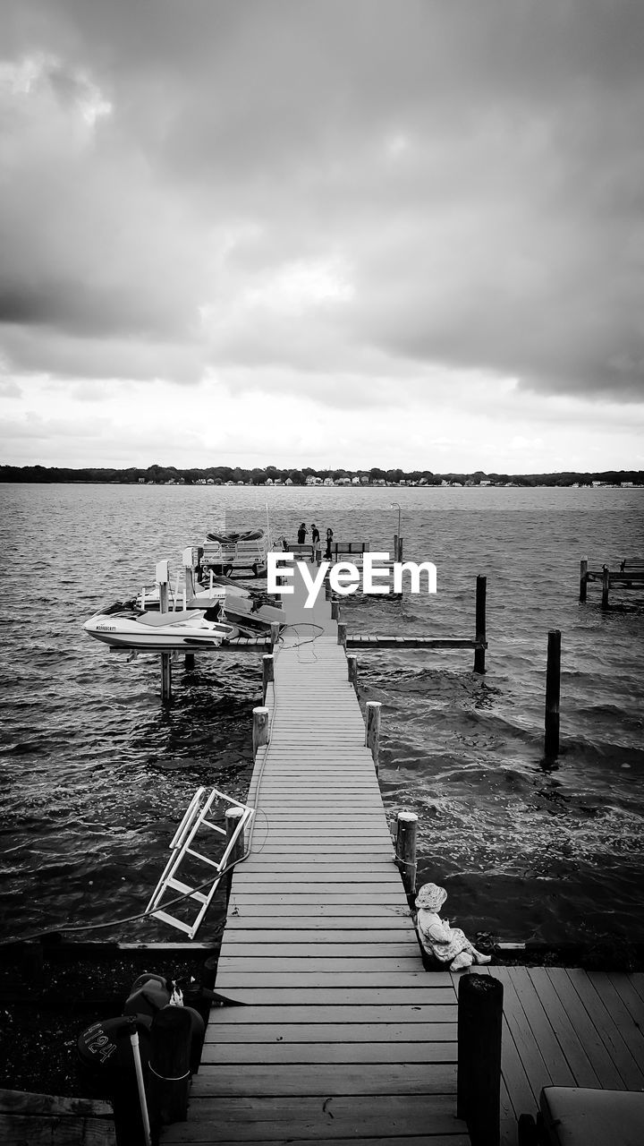 Wooden pier on sea against cloudy sky