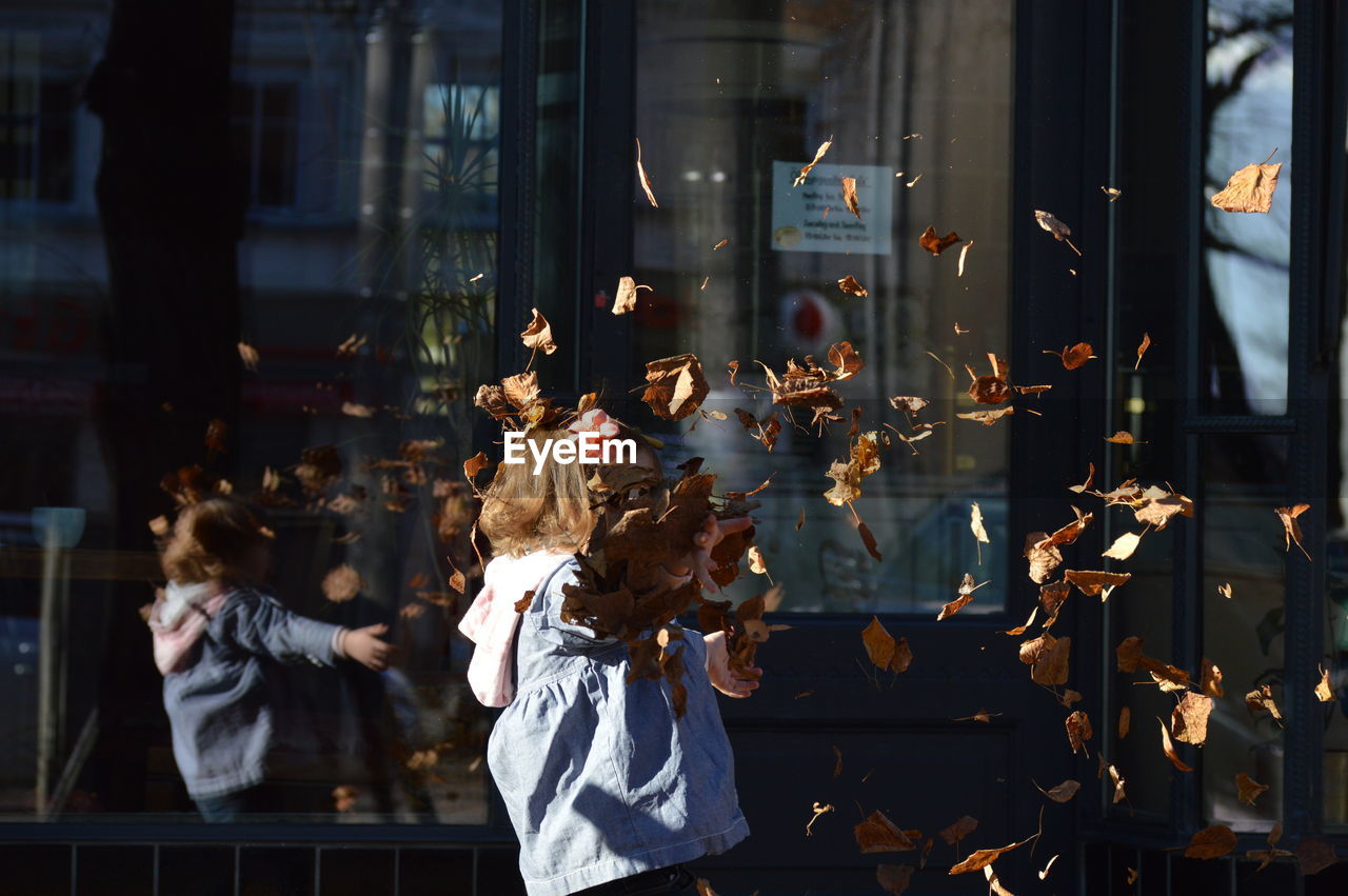 Girl throwing dry leaves in mid-air at city