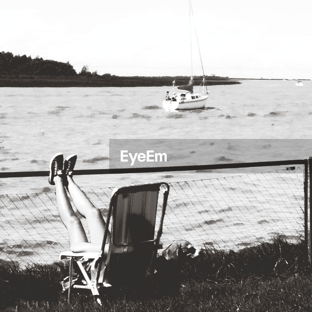 Woman sitting on chair with legs on fence against sea