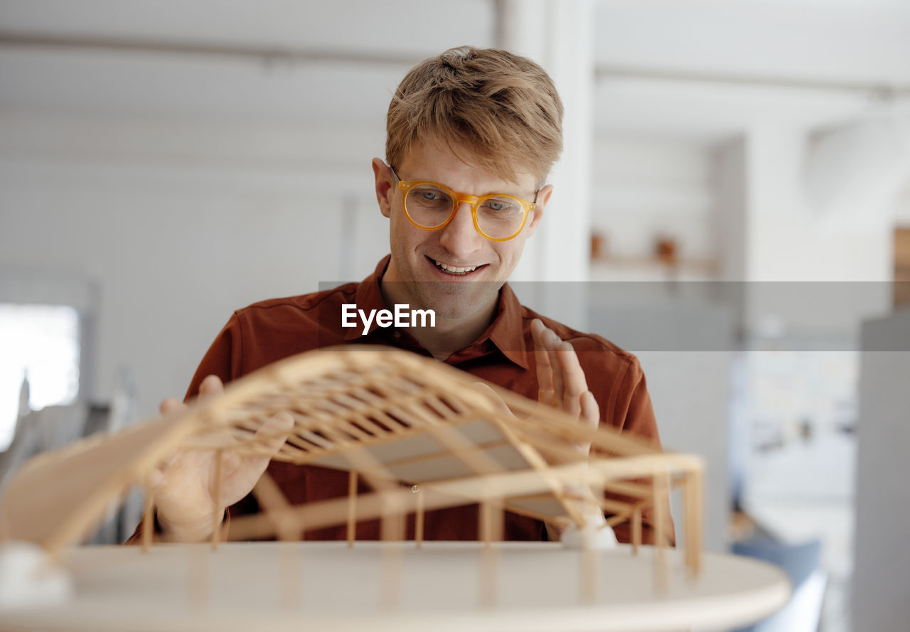 Smiling architect wearing eyeglasses looking at leaf shaped model in office