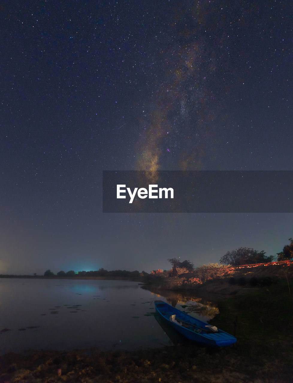 Rowboat on lakeshore against star field sky