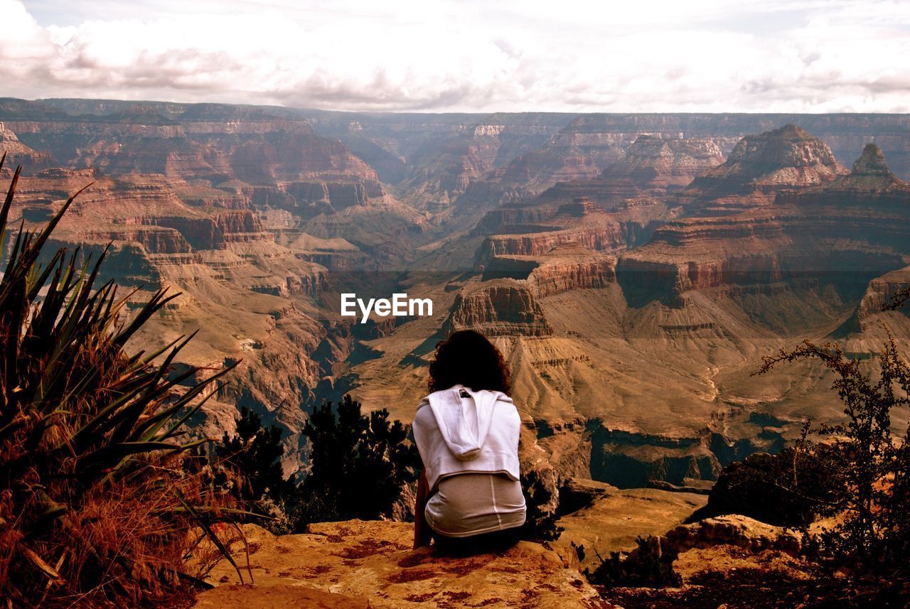 Rear view of woman sitting on rock against sky