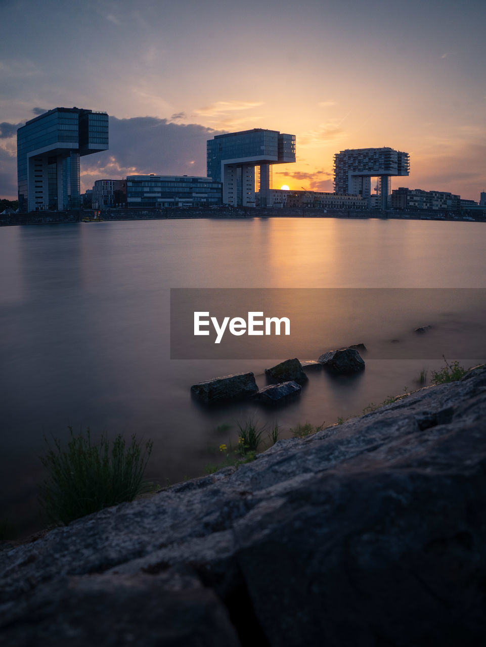 Scenic view of river by buildings against sky at sunset