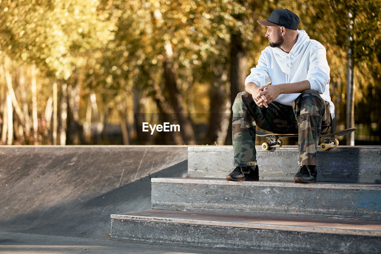 Man sitting with skateboard on staircase at park