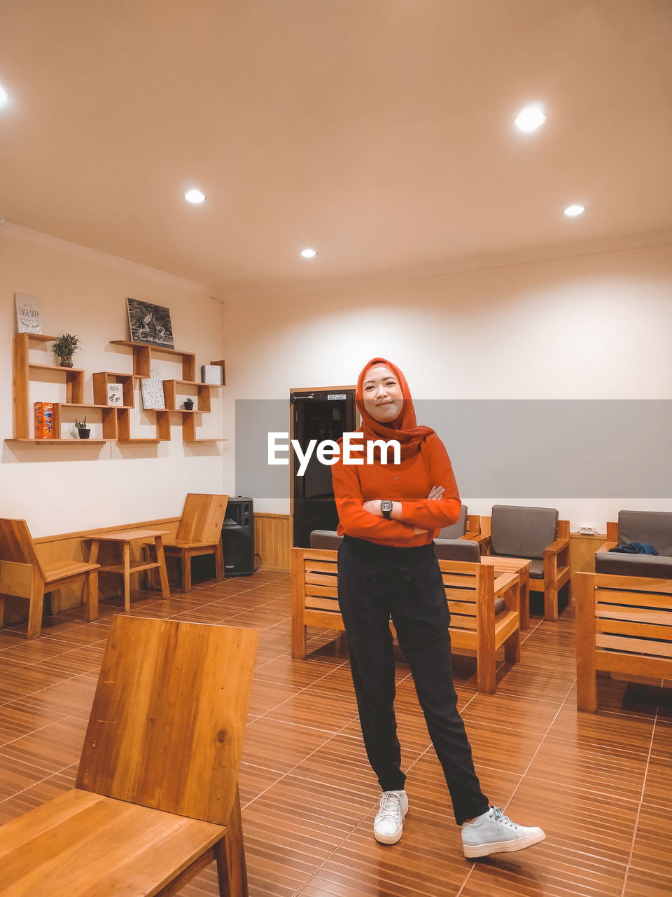 PORTRAIT OF SMILING YOUNG WOMAN STANDING IN ILLUMINATED ROOM