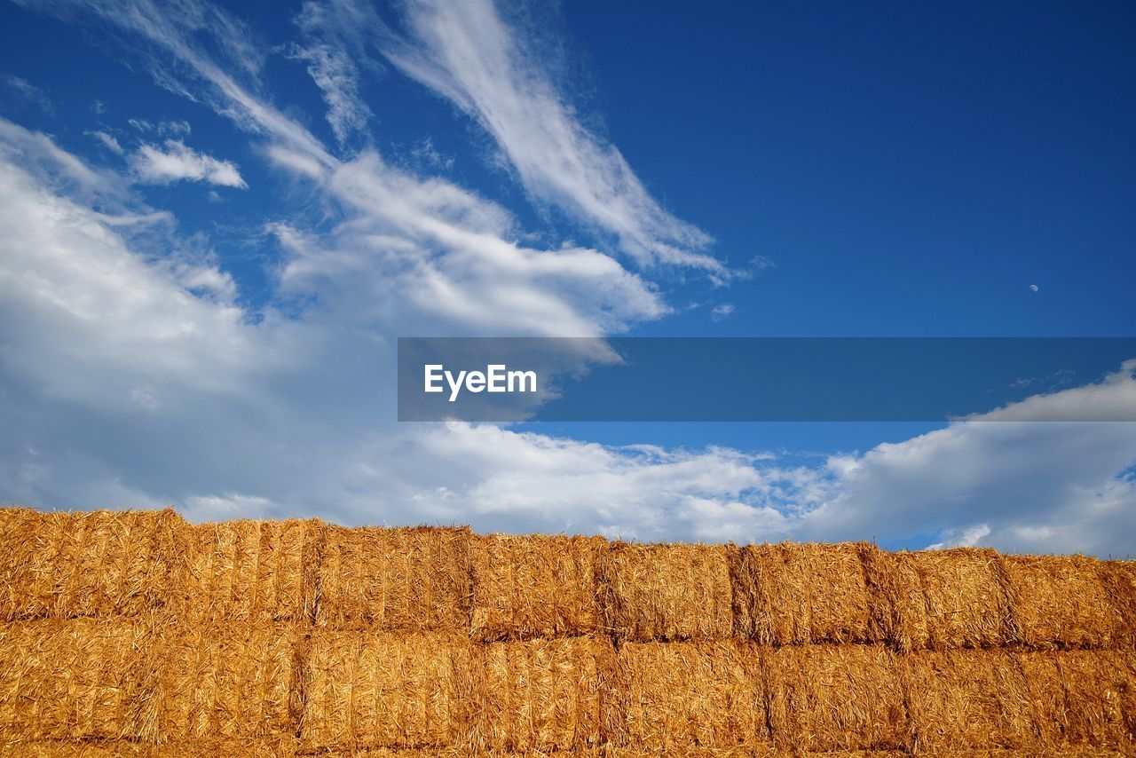 Low angle view of hay bales against cloudy blue sky on sunny day