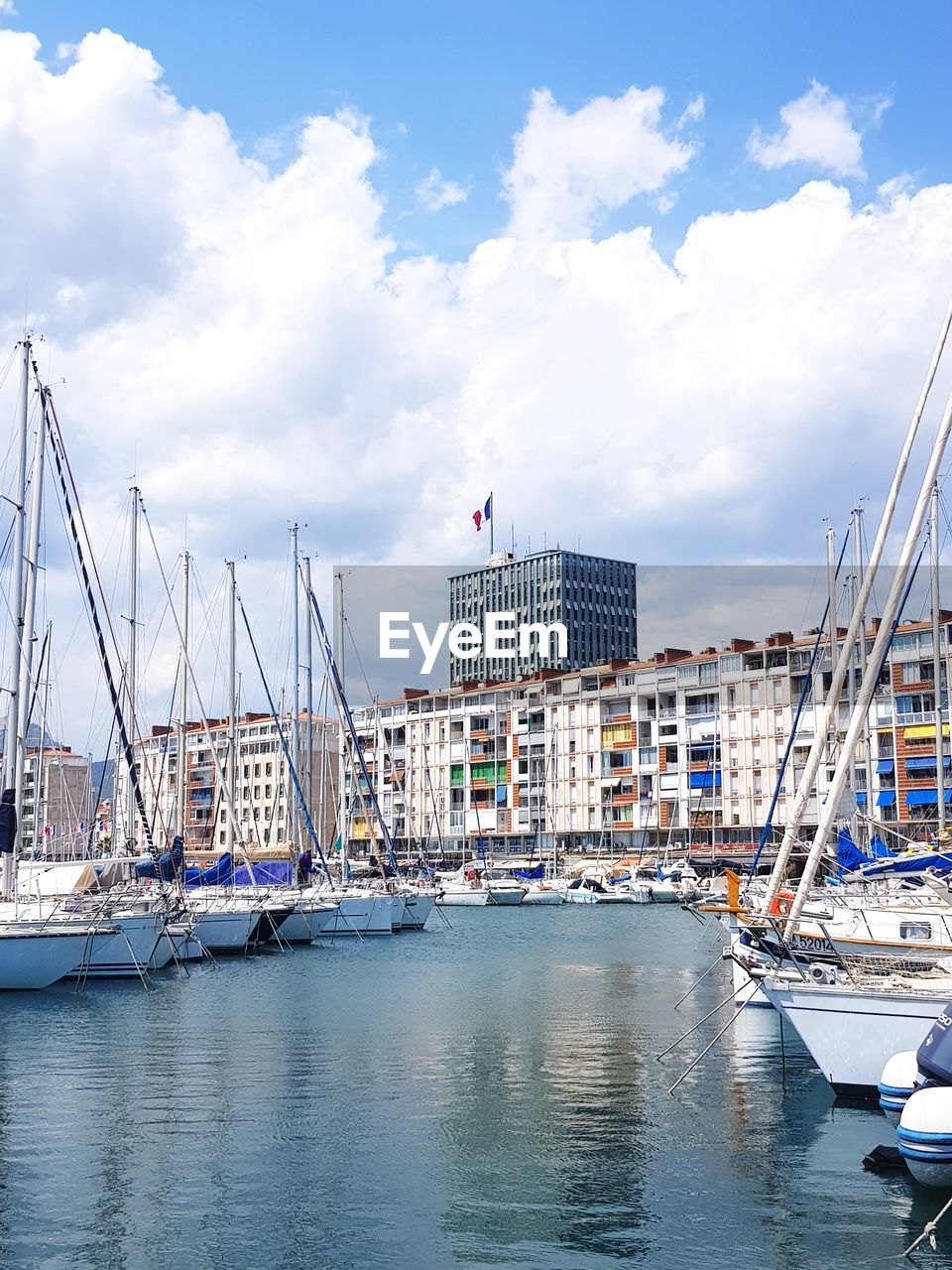 Sailboats moored on harbor by buildings against sky