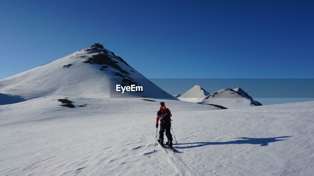 Rear view of person skiing on snowcapped mountain against clear sky