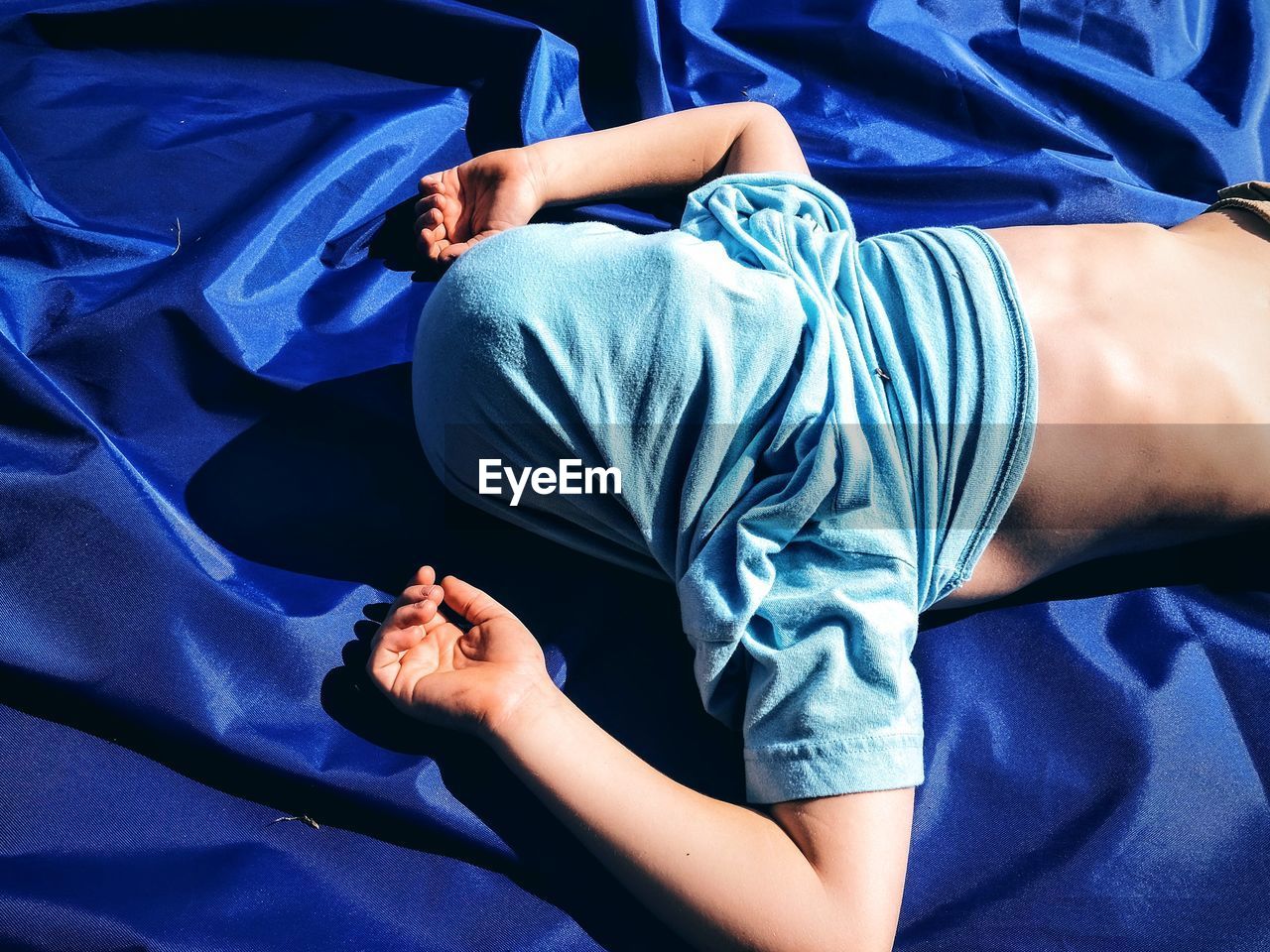 High angle view of boy with covered face sleeping on blue fabric in yard
