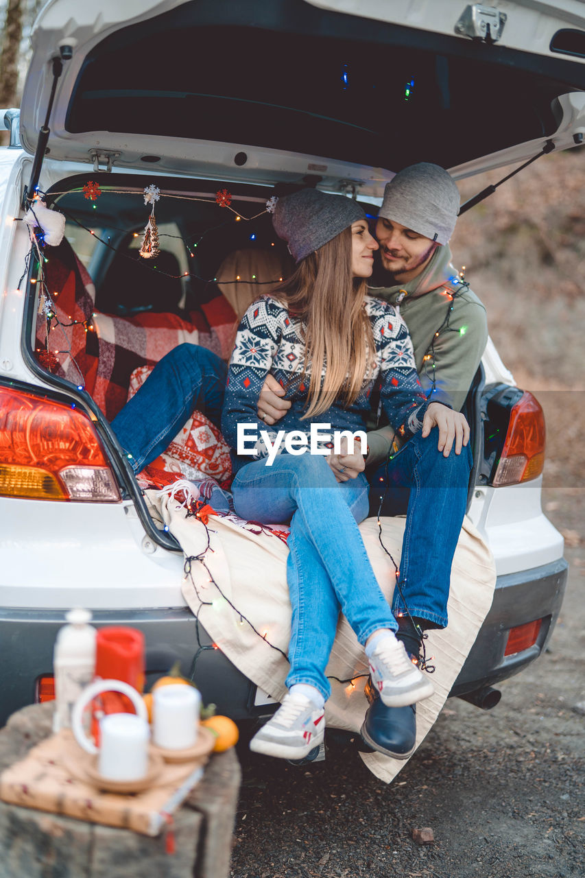 Smiling couple embracing while sitting in car trunk