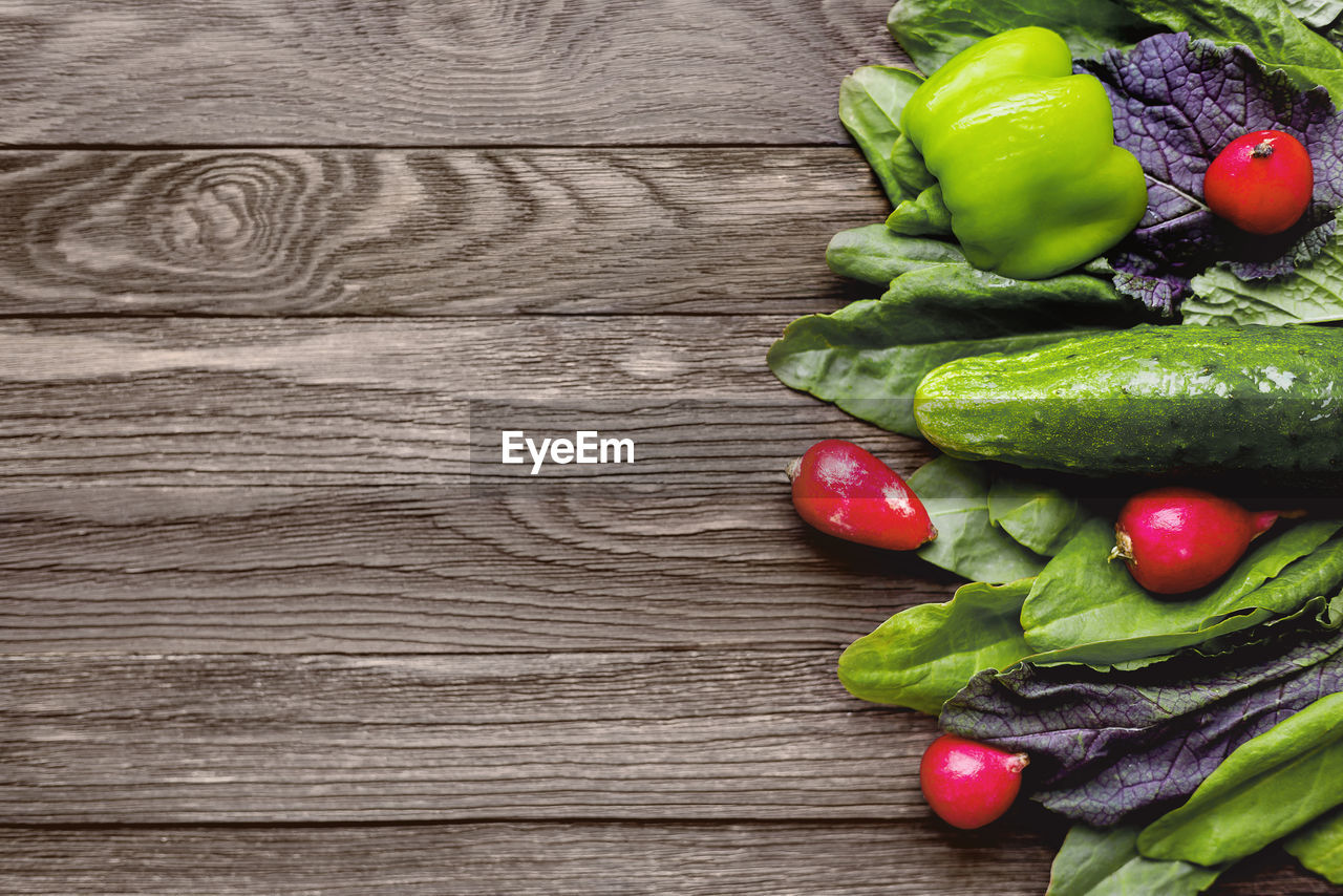 Fresh ingredients for salad - sorrel leaves, radishes, cucumber, sweet pepper on wooden background.