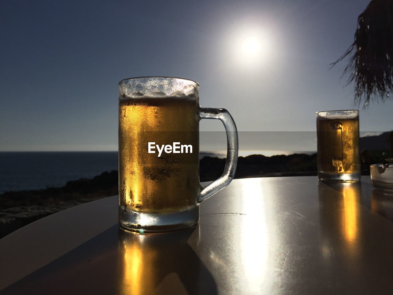 CLOSE-UP OF BEER ON TABLE AGAINST SEA DURING SUNSET
