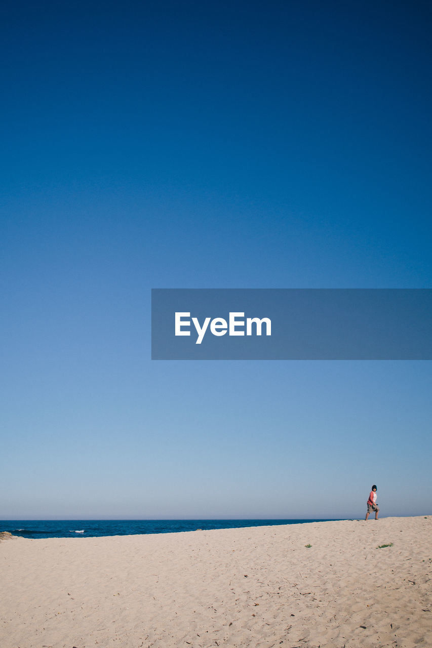 Woman walking on sand at beach against clear blue sky