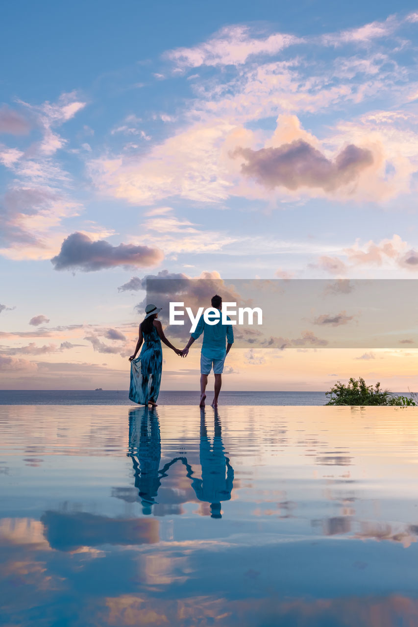 rear view of woman standing on beach against sky during sunset