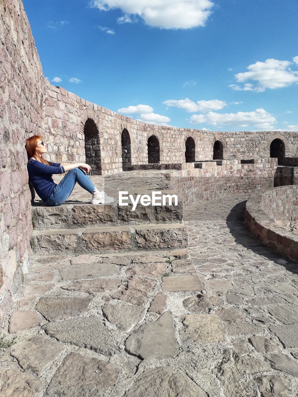 Woman sitting at historical building against sky