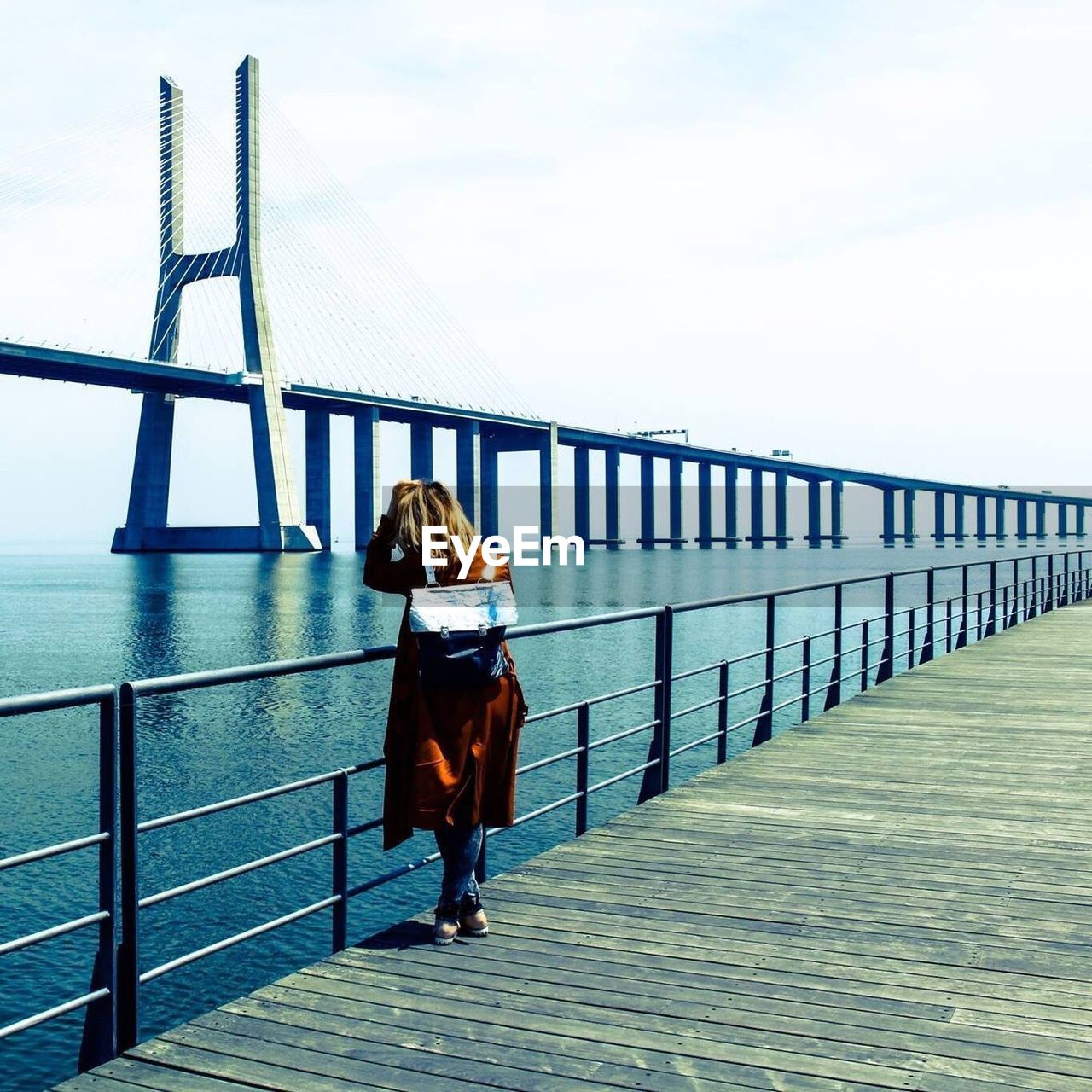 Rear view of woman standing on pier against vasco da gama bridge over sea