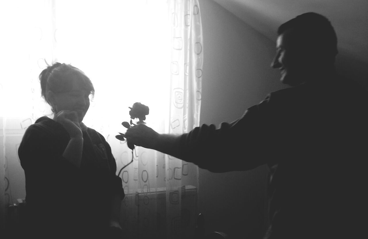 Smiling young man giving flower to girlfriend at home