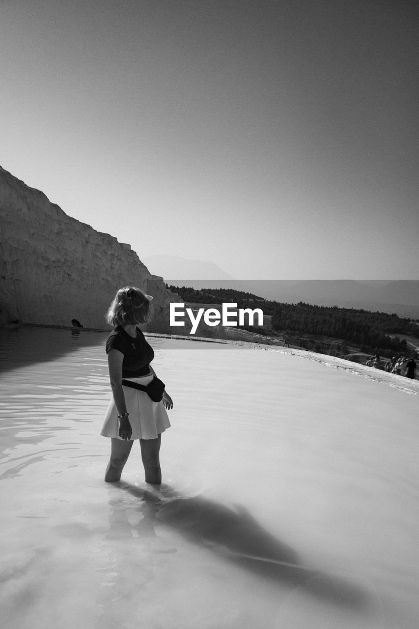 Woman standing in hot spring against clear sky