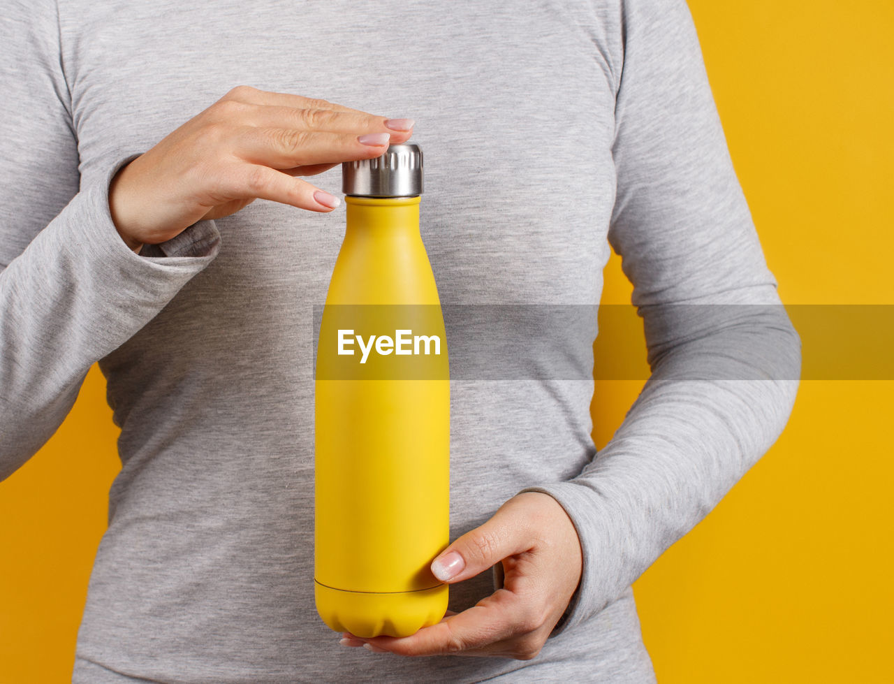 Close up of woman in grey tee holding yellow insulated bottle on yellow background