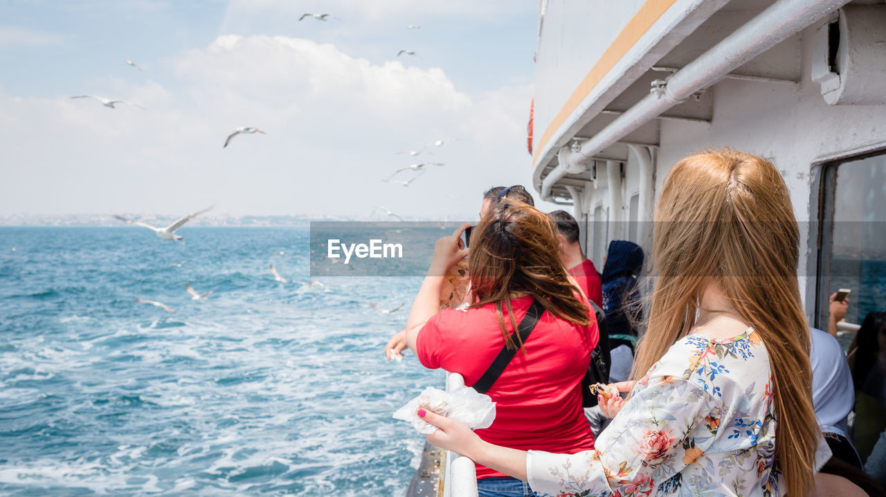 REAR VIEW OF WOMEN LOOKING AT SEA