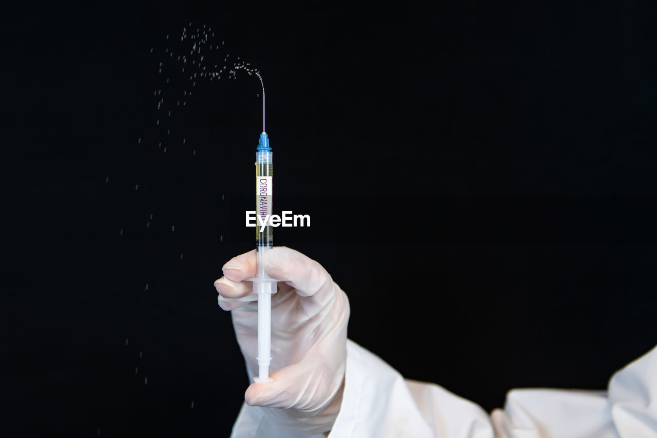 Cropped hand of doctor holding syringe against black background