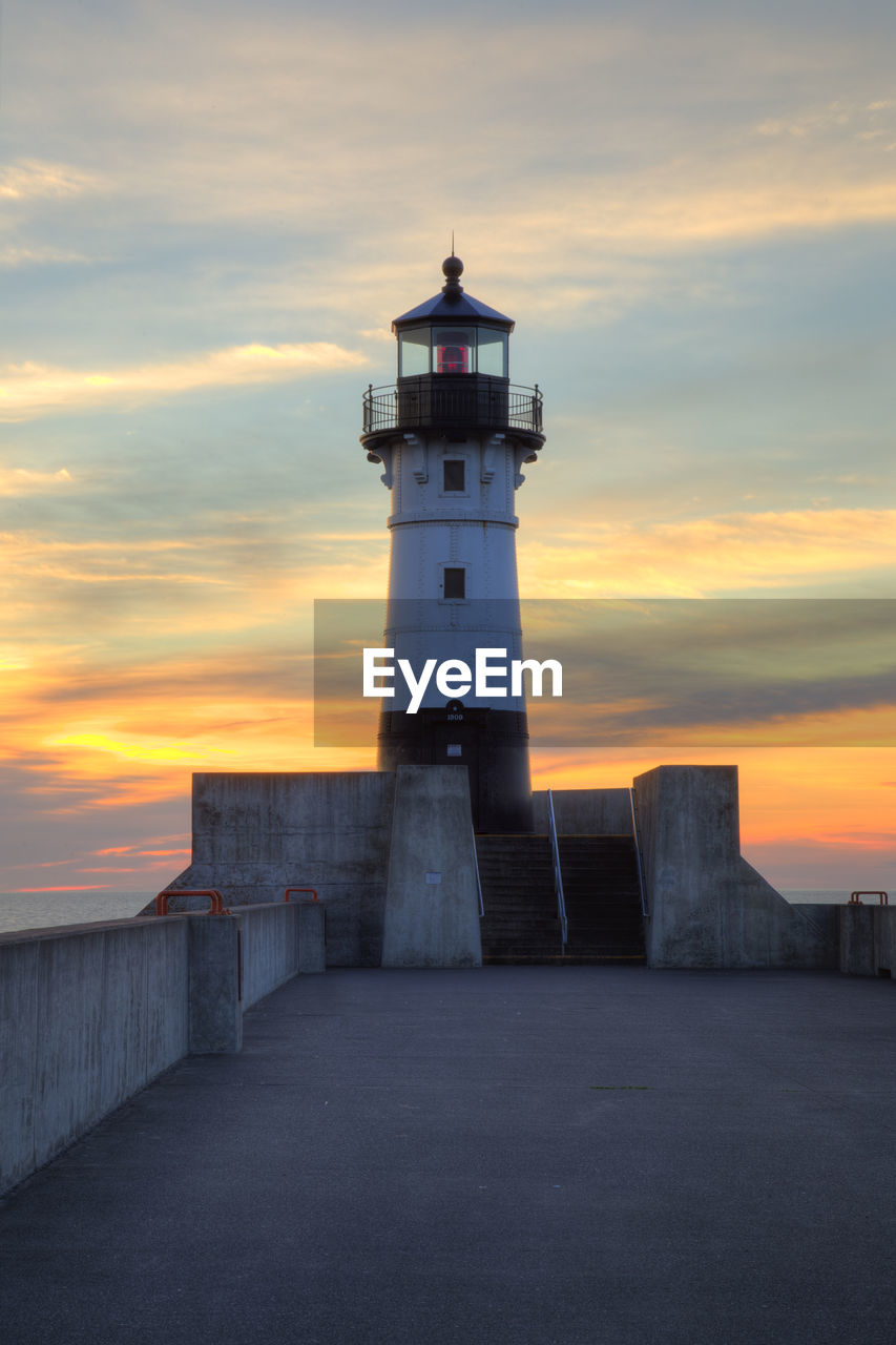 Lighthouse by sea against sky during sunset