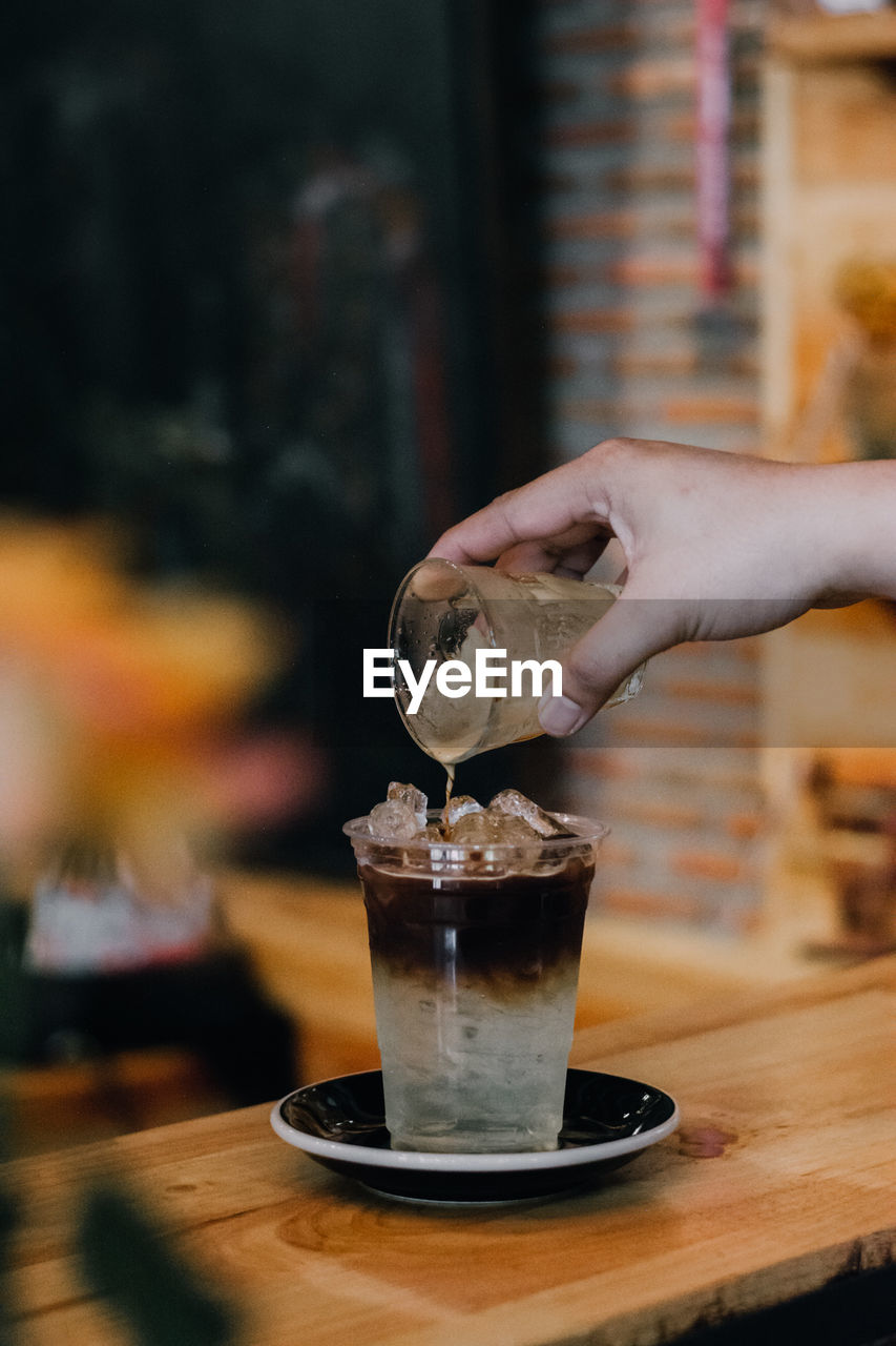 Cropped hand pouring drink in glass on wooden table