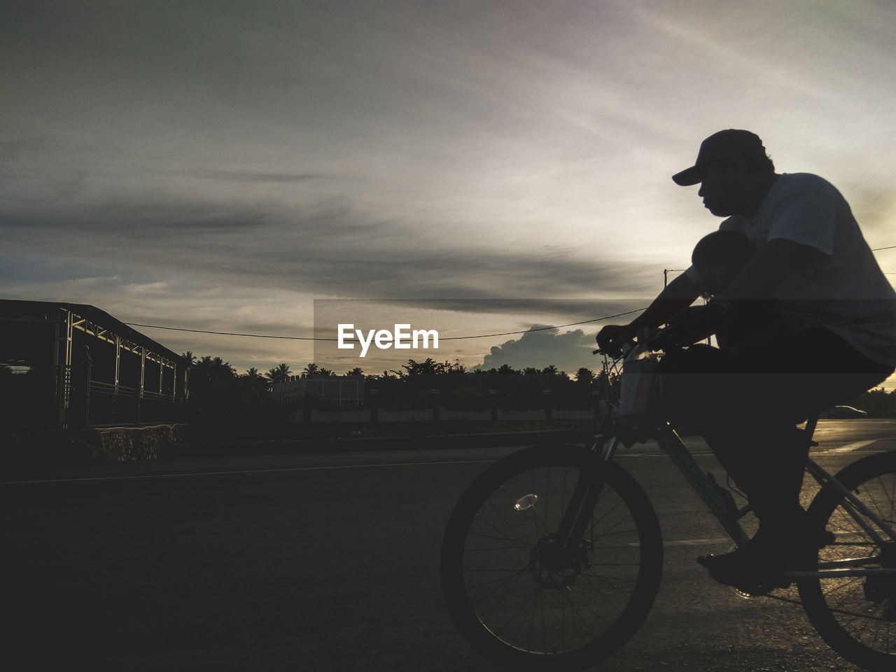 Silhouette father with son riding bicycle on road against sky during sunset