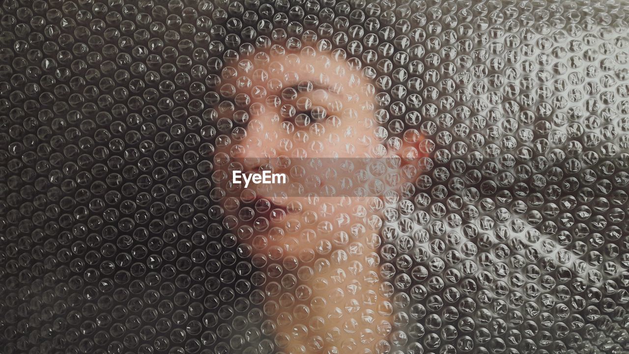 Close-up portrait of young woman seen through bubble wrap