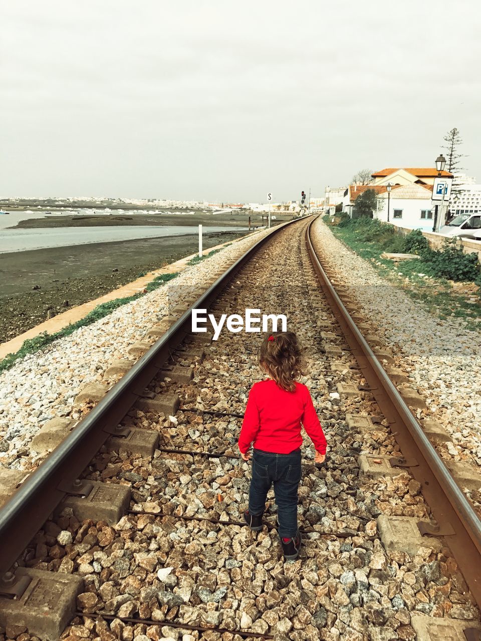 Full length rear view of girl walking on railroad track against clear sky