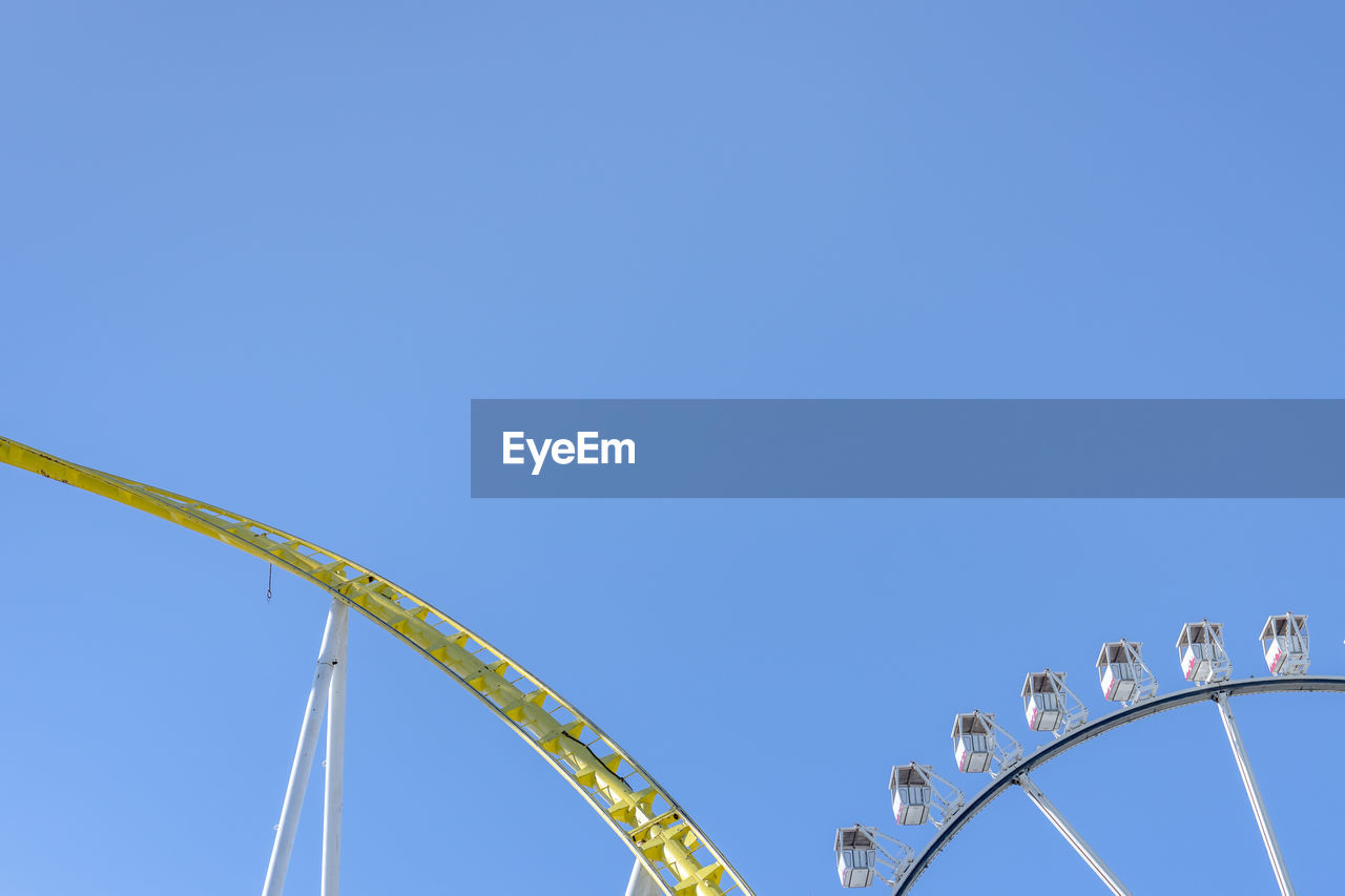 Low angle view of rollercoaster against clear blue sky