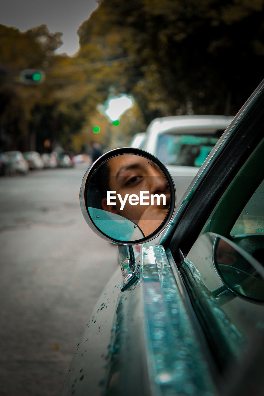 Portrait of young man reflecting on side-view mirror while traveling in car