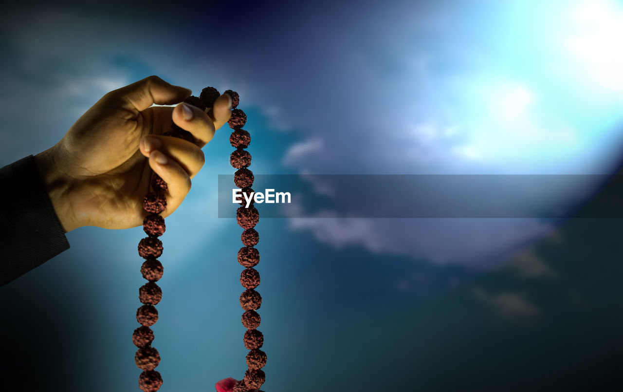 Prayer beads in hand isolated on sky with rays. hand holding rosary, praying god, religious theme