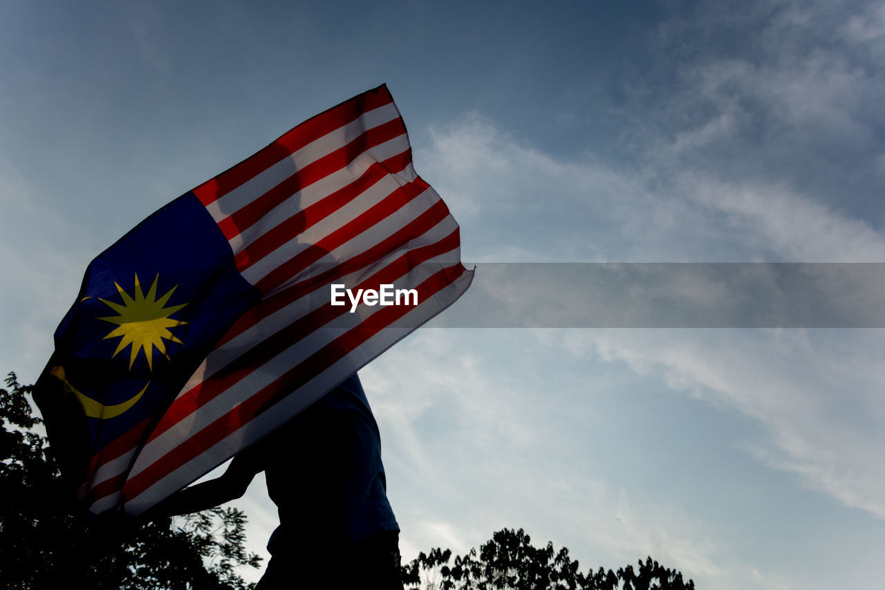 Low angle view of man with malaysian flag standing against sky