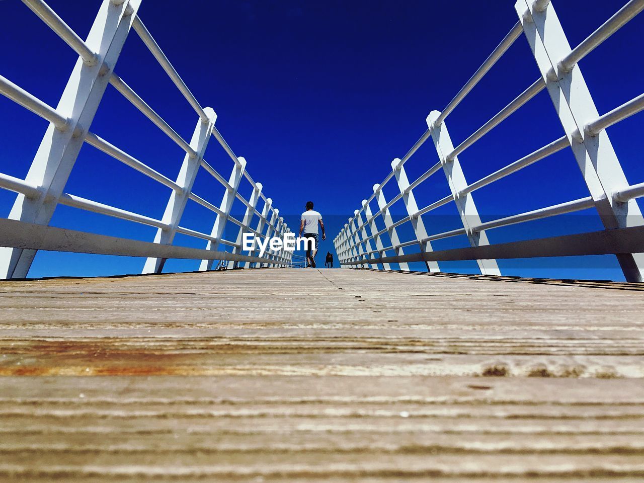 Low angle view of woman on footbridge against clear blue sky